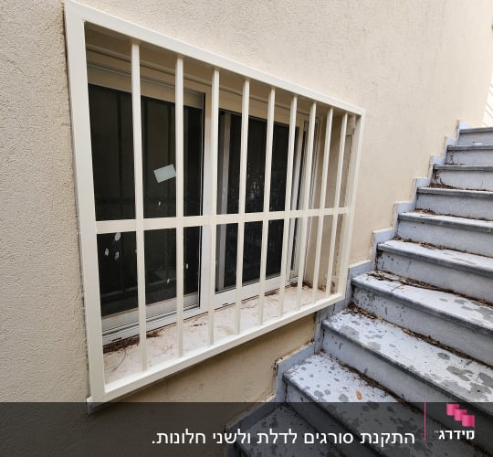 חלון עם סורגים לבנים ליד מדרגות בטון